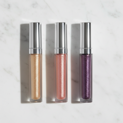 Three glitter liquid eyeshadow tubes in champagne gold, rose pink and violet purple laid flat on marble surface
