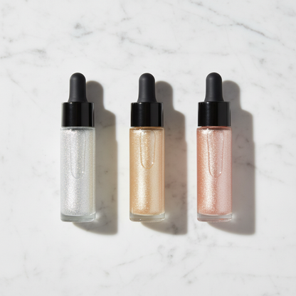 Three clear glass dropper bottles with silver white, champagne gold and rose gold glitter highlighter on marble surface